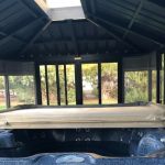 Covered hot tub inside a gazebo with glass windows and a pitched roof.