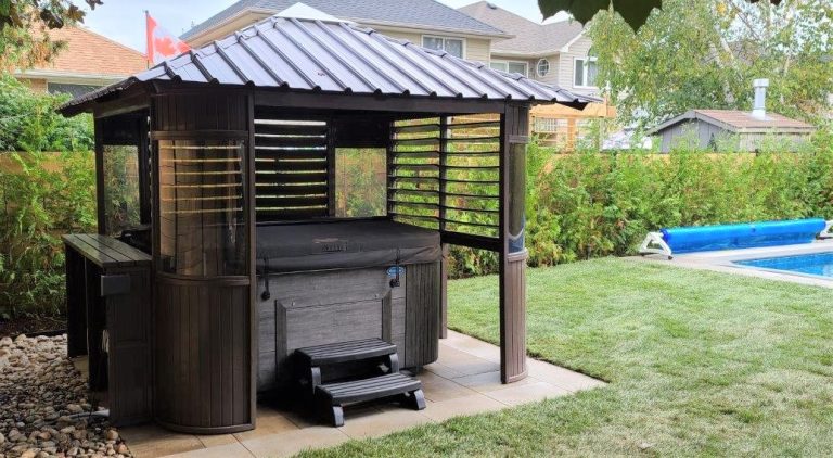 Gazebo with hot tub in a leafy backyard beside a pool and Canadian flag.