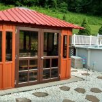 Small wooden gazebo with red roof next to a swimming pool, surrounded by stepping stones and greenery.