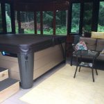 Indoor hot tub with steps, next to a sofa with colorful pillows, a small table, and a rug in a room with large windows.