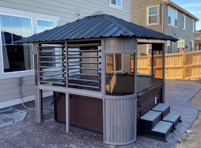 Wooden gazebo enclosure over a hot tub with steps, near a house and fenced yard.