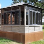 Small garden gazebo with glass windows and a metal roof in a grassy yard.
