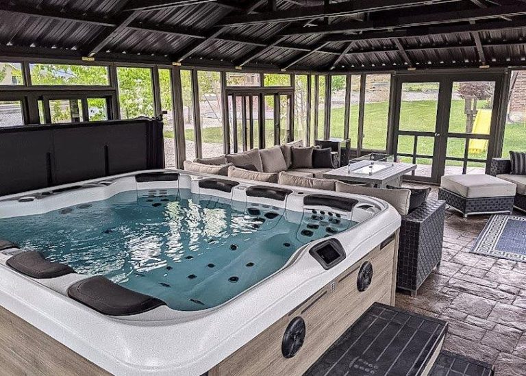 Indoor gazebo with a large hot tub, surrounded by wicker furniture and glass doors.