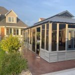 A patio with a screened gazebo next to a two-story house, surrounded by green lawn and bushes on a sunny day.