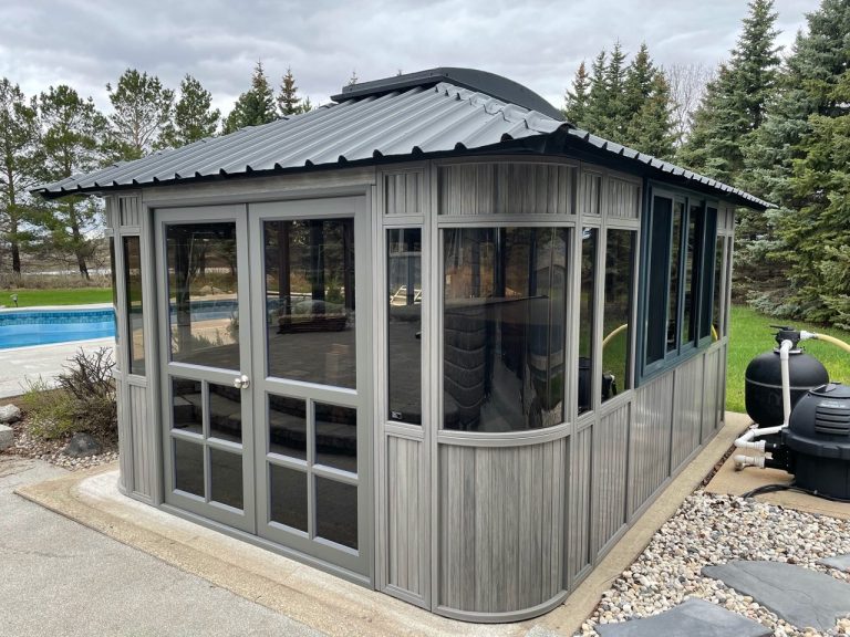 A modern gray garden shed with large windows, near a pool and surrounded by trees.