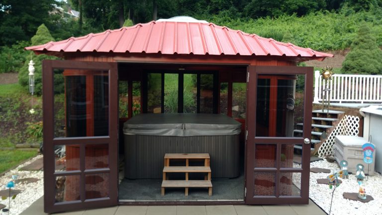 Gazebo with red roof and open doors revealing a covered hot tub inside, surrounded by a garden and decorative items.