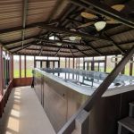 Covered outdoor swim spa with a gabled roof, surrounded by windows, and steps leading to the spa.