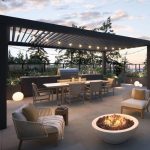 Modern outdoor patio with a pergola, dining table, chairs, grill, fire pit, and string lights at sunset.