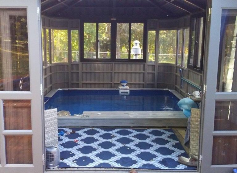 Small indoor pool inside a wooden gazebo with glass windows and a patterned rug on the floor.