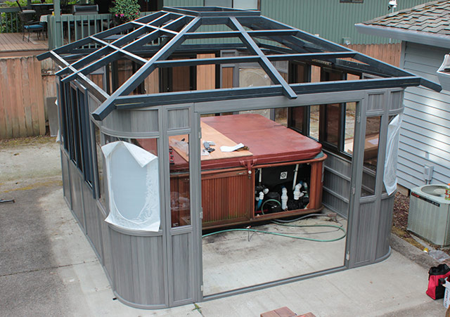 Outdoor gazebo under construction with a hot tub inside, partially enclosed with glass panels and framework.