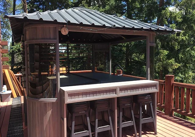 Gazebo-style hot tub with bar stools on a wooden deck surrounded by trees.