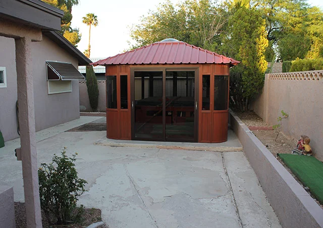 Red-roofed gazebo in a backyard with concrete path and surrounding trees.
