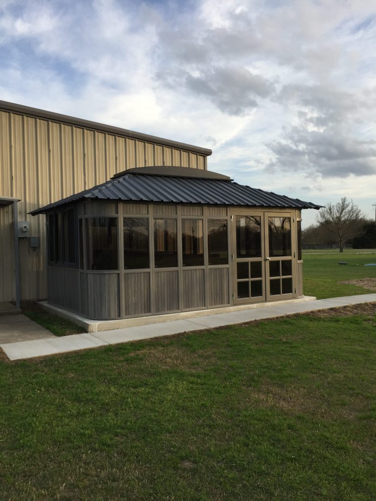 Metal-roofed, glass-walled extension attached to a beige corrugated building under a cloudy sky.