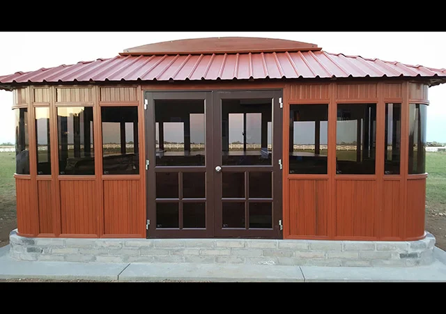 Wooden gazebo with large windows and a red metal roof on a concrete base.