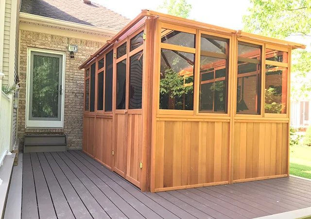 Wooden screened gazebo on a house deck, adjacent to a brick wall with a glass door.