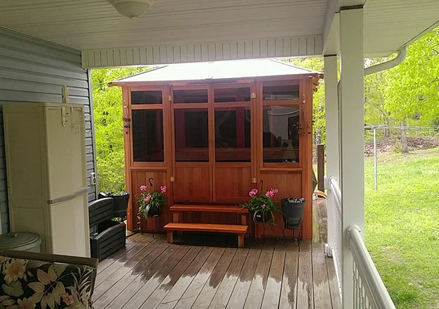 Wooden gazebo with glass windows on a covered deck, surrounded by potted plants.