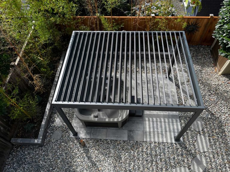 Aerial view of a pergola over a hot tub, surrounded by gravel and greenery in a backyard setting.
