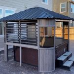 Wooden gazebo enclosure over a hot tub with steps, near a house and fenced yard.