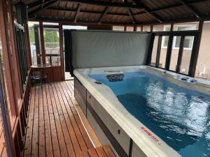 Indoor hot tub in a wood-paneled room with large windows and a small table in the corner.
