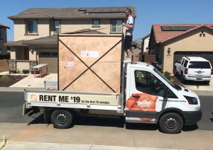 Person standing on a truck next to a large wooden crate in a residential neighborhood.