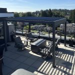Rooftop patio with pergola, seating area, potted plants, and city view under a clear blue sky.