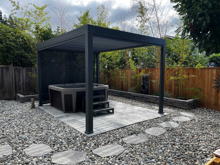 Outdoor hot tub under a modern pergola, surrounded by pebbles and stepping stones, bordered by bamboo and wooden fencing.