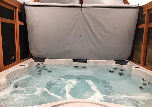 Bubbling hot tub with an open cover inside a wooden enclosure.