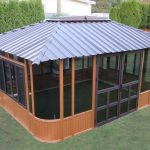 A wooden garden gazebo with glass windows and a metal roof on a green lawn.