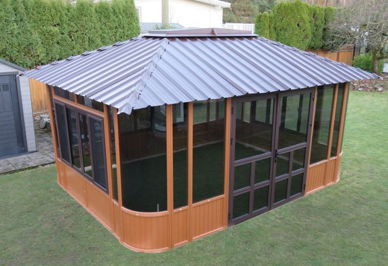 A wooden garden gazebo with glass windows and a metal roof on a green lawn.