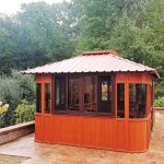 Wooden gazebo with a red roof on a patio, surrounded by trees.