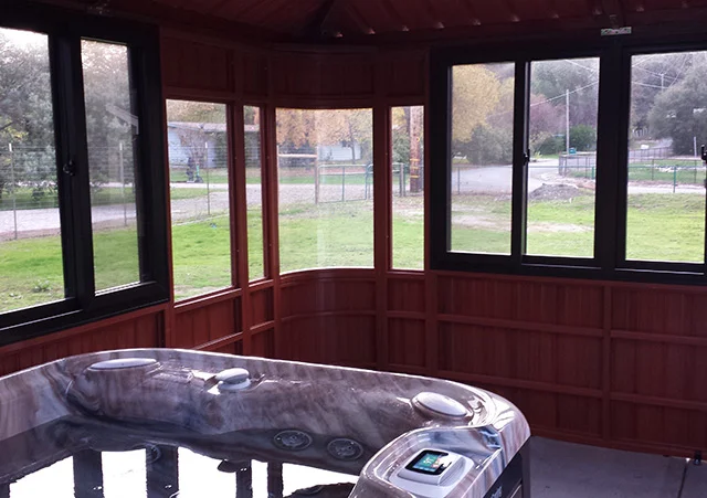 Indoor hot tub in a wooden room with large windows overlooking a grassy outdoor area.