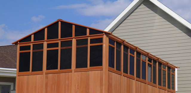 Wooden screened porch extension attached to a house exterior under a partly cloudy sky.