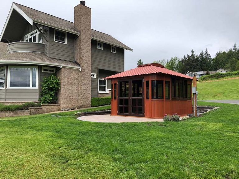 Two-story gray house with a chimney and an orange gazebo on a lawn under a cloudy sky.