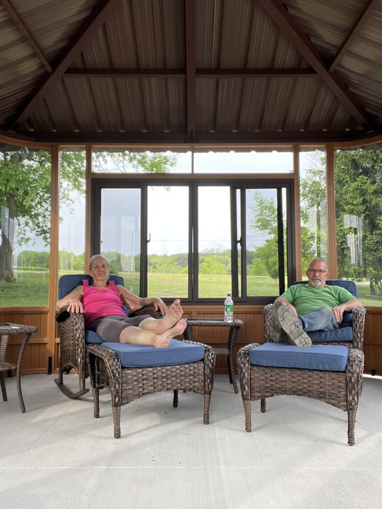 Two people relaxing on wicker chairs in a gazebo with visible greenery outside.